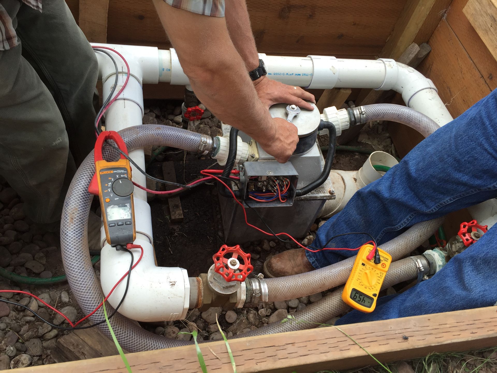 Two people working on water pump system with electrical meters and pipes.