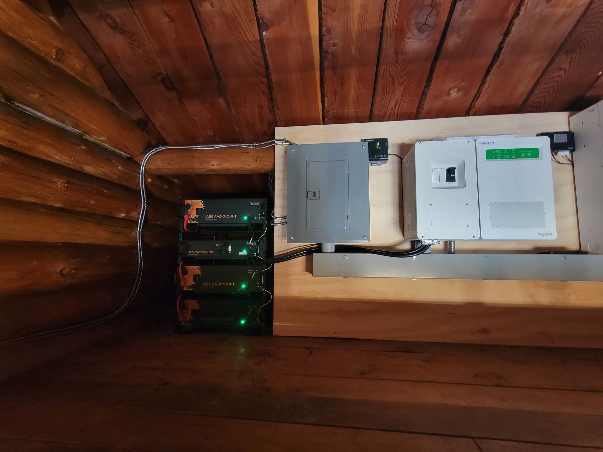 Electrical equipment: stacked black boxes, gray panel, and white inverter mounted on wooden boards in an attic.