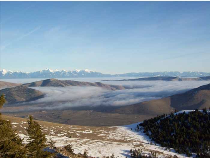 Hills and mountains in a winter landscape with fog filling the valleys, under a blue sky.