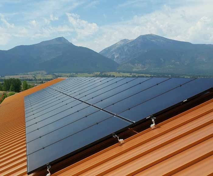 Solar panels on a rust-colored metal roof, with mountains and sky in the background.