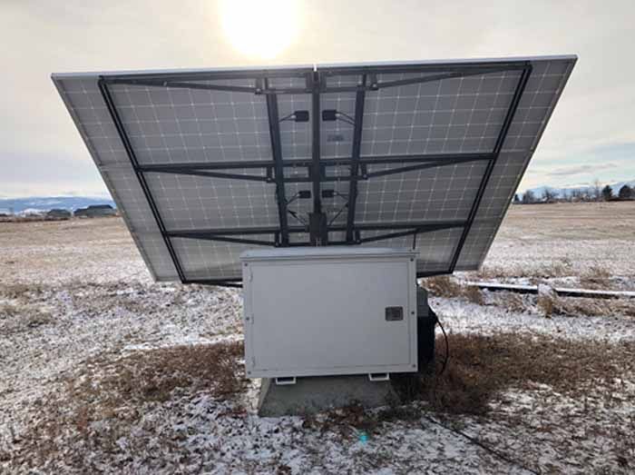Solar panel array mounted on a white box in a snowy field with the sun in the background.