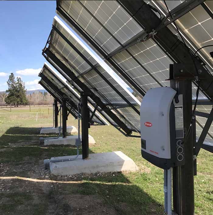 Solar panels mounted on metal frames in a field with an attached inverter.