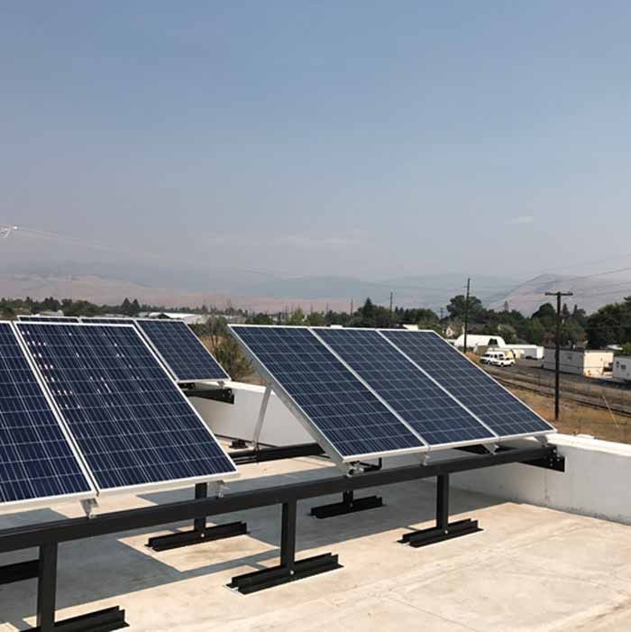 Solar panels installed on a flat roof with a view of a town and mountains in the background.