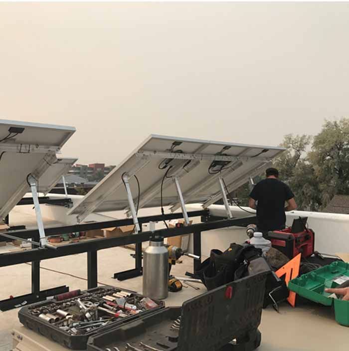 Solar panels being installed on a flat roof by a worker with tools.