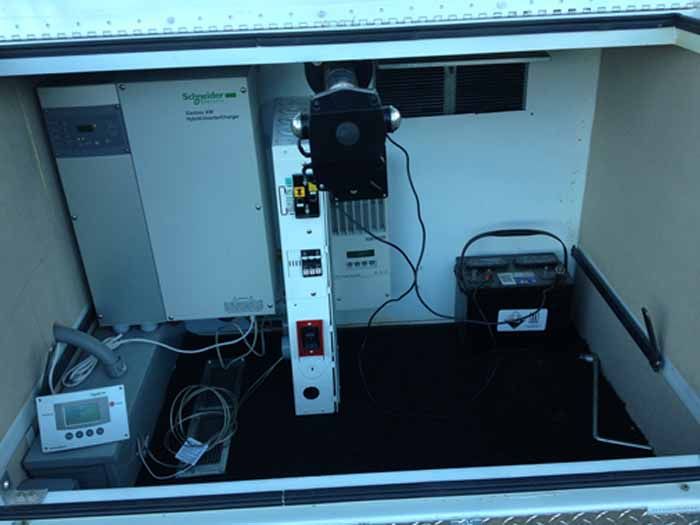 Interior of a utility box with electrical equipment: inverter, charger, batteries, and control panels.