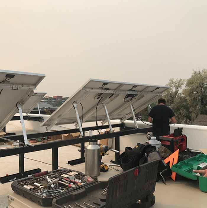 Solar panel installation on a rooftop; worker, tools, panels in progress; overcast sky.