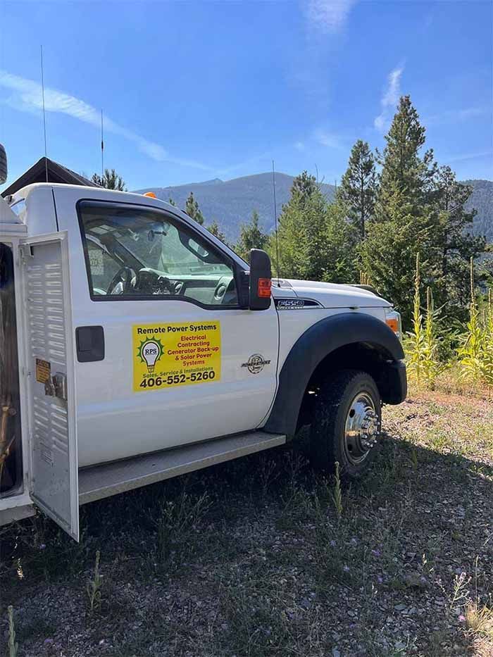 White work truck parked outdoors with business logo; mountains and trees in background.