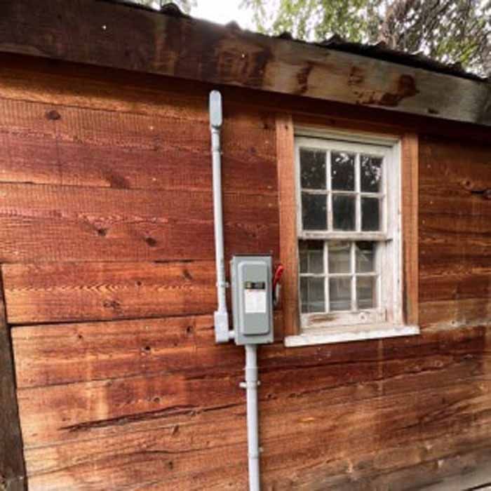 Wooden building with white-framed window. Gray electrical conduit and box attached to the exterior.