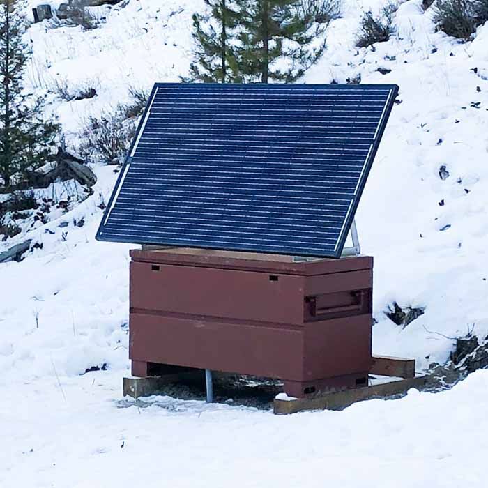 Solar panel on a brown wooden box, set in a snowy, outdoor environment.