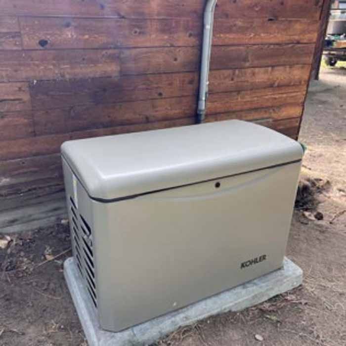 Gray Kohler generator on a concrete pad next to a wooden building.