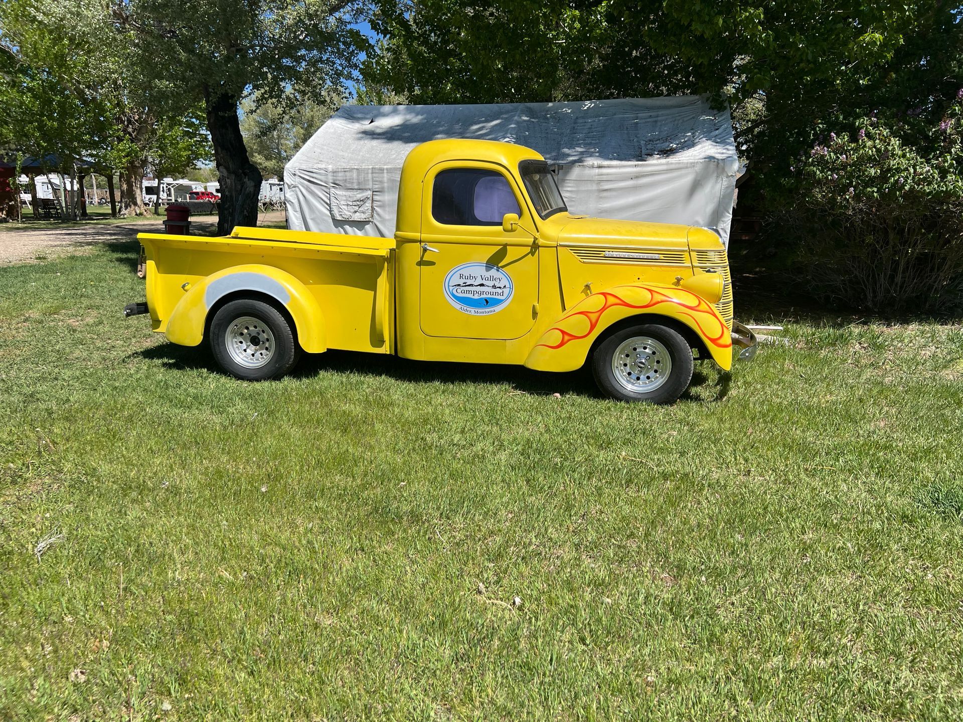A yellow truck is parked in the grass next to a tent.