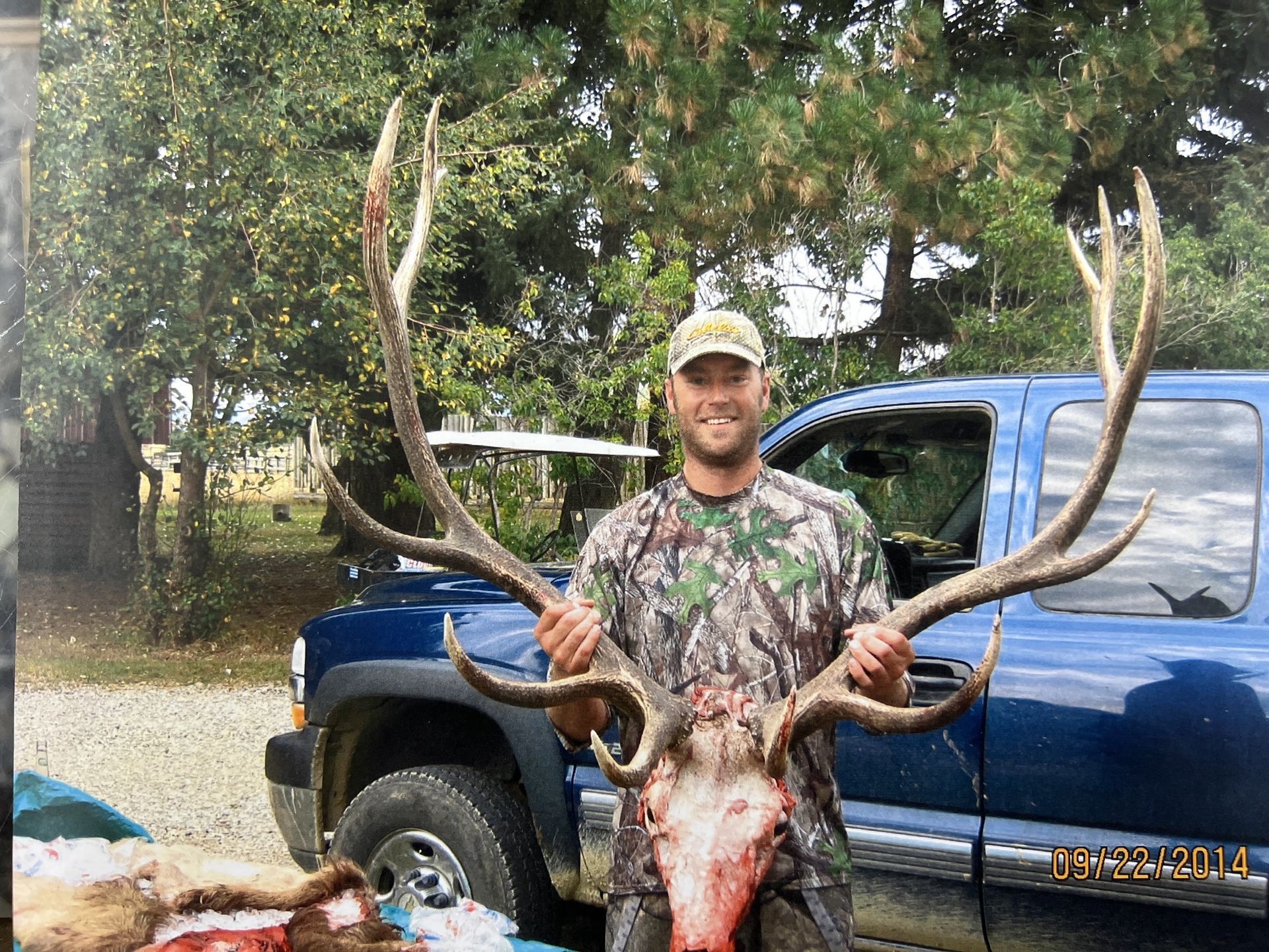 A man is holding a large deer head in front of a blue truck.