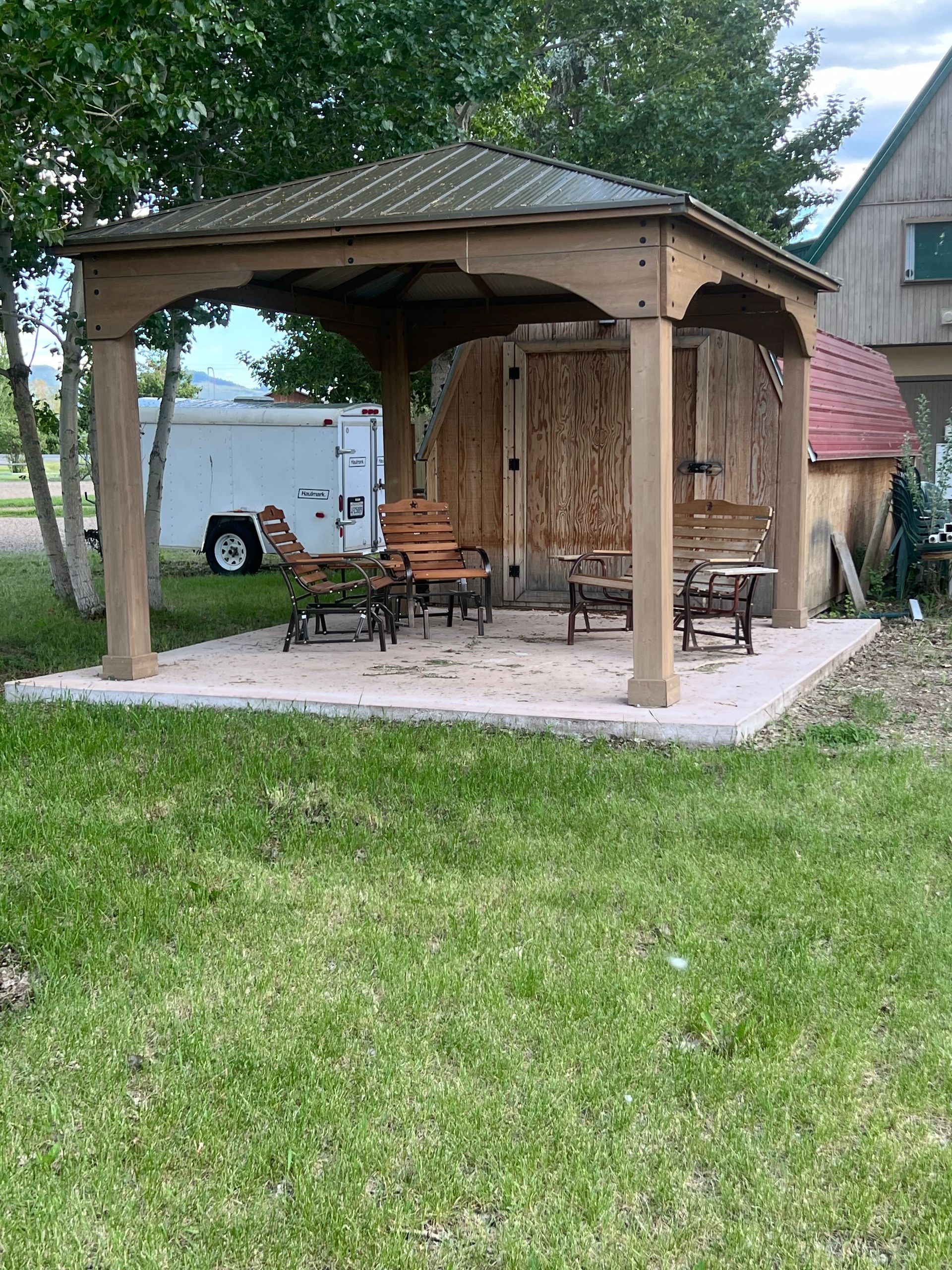 A wooden gazebo with chairs and a table in a grassy yard.