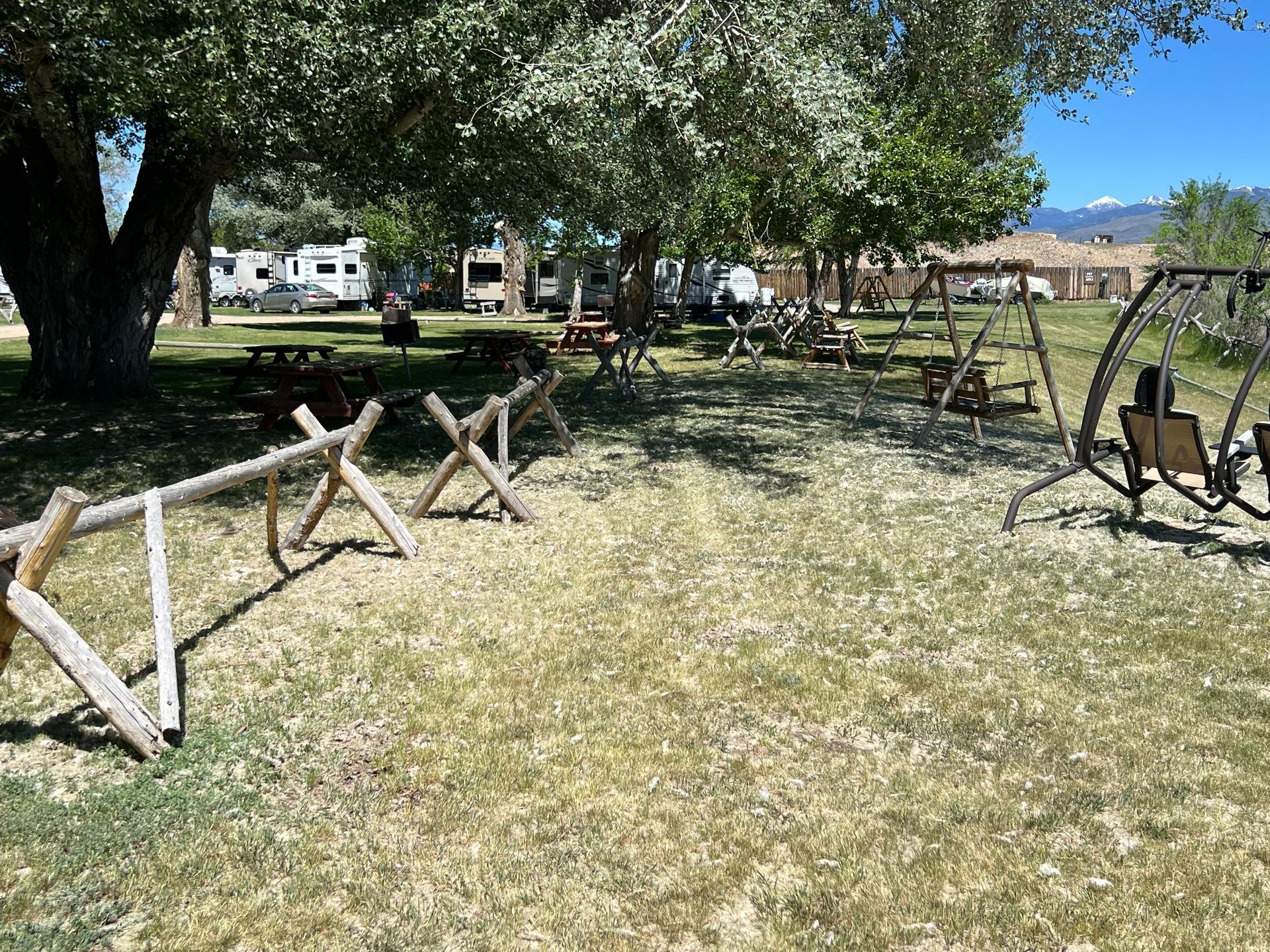A park with a wooden fence , swings , tables and trees.