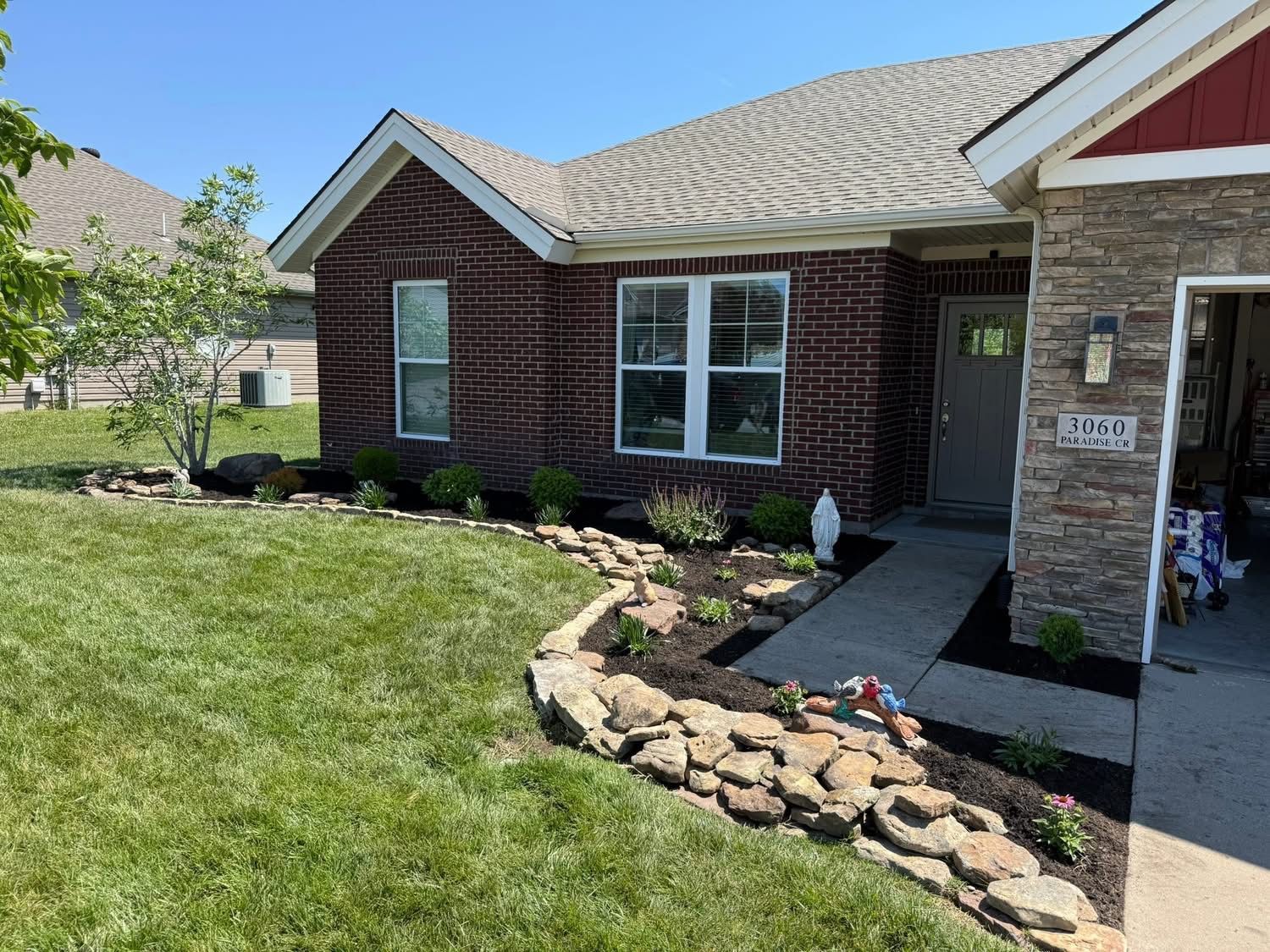 Brick suburban house with a stone-lined garden bed and concrete walkway leading to the front door.