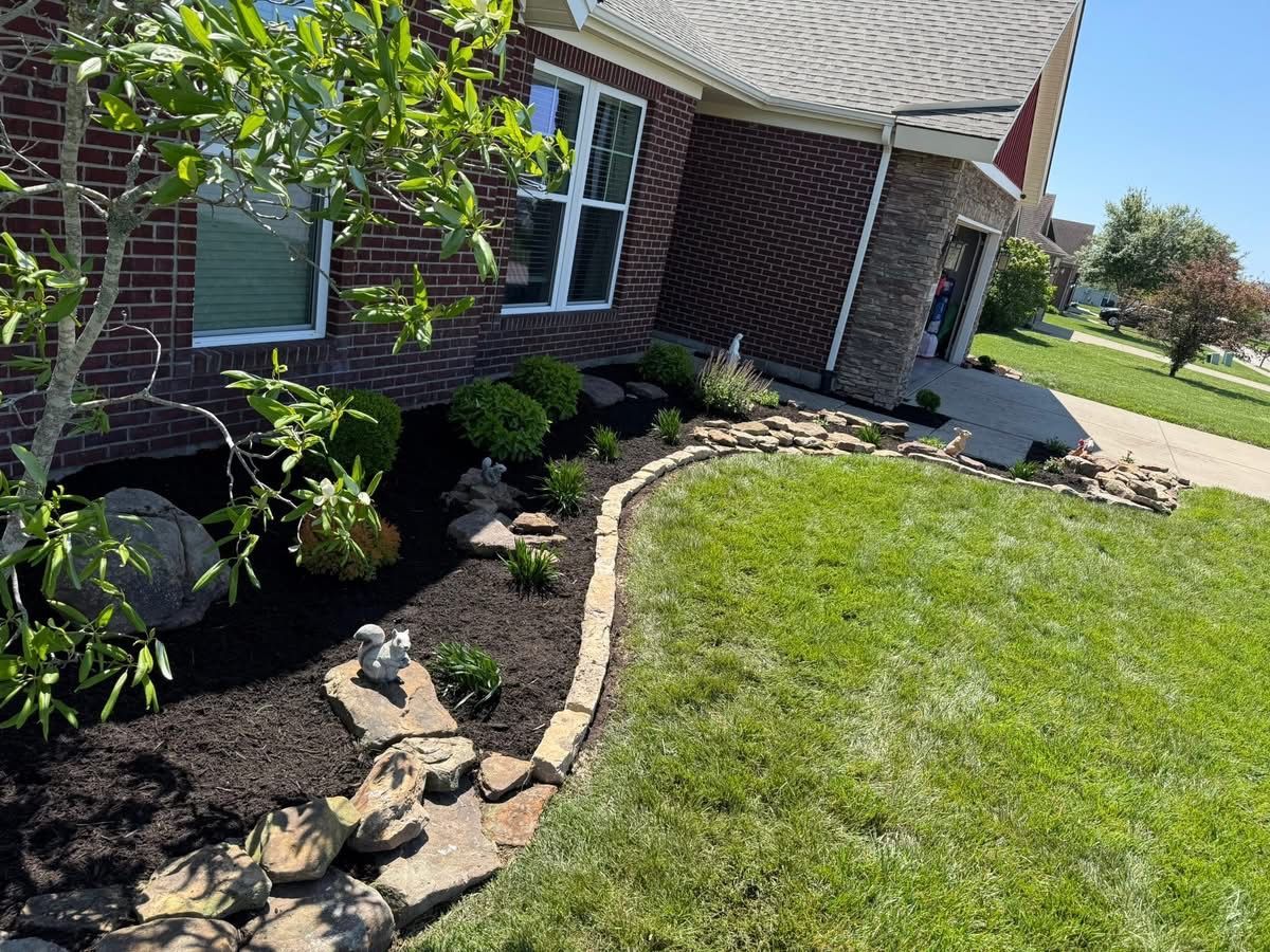 Brick house front yard with curved stone border, mulch bed, shrubs, and green lawn
