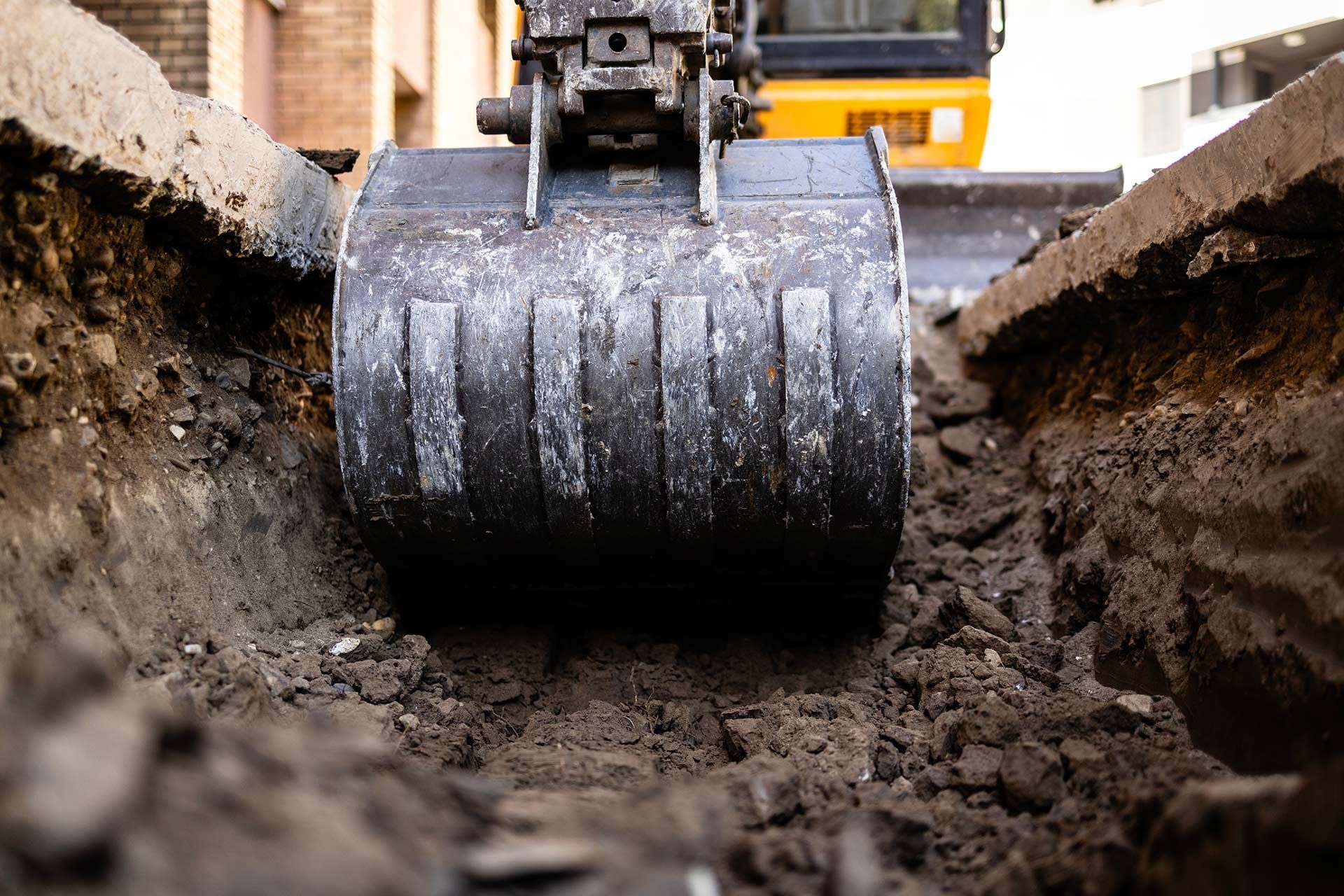 Excavator bucket digging a trench in the ground, close-up view.