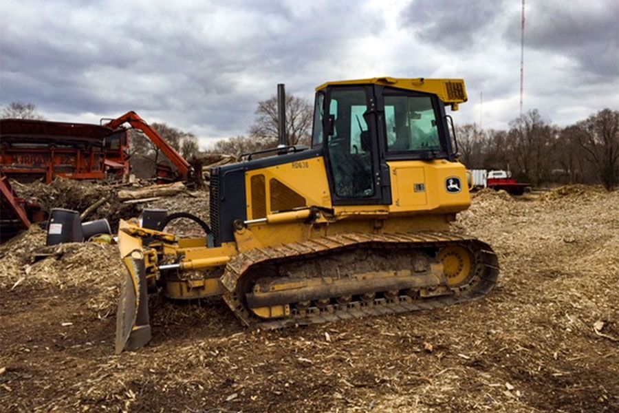 Yellow John Deere bulldozer clearing wood chips. Cloudy sky, wooded setting.