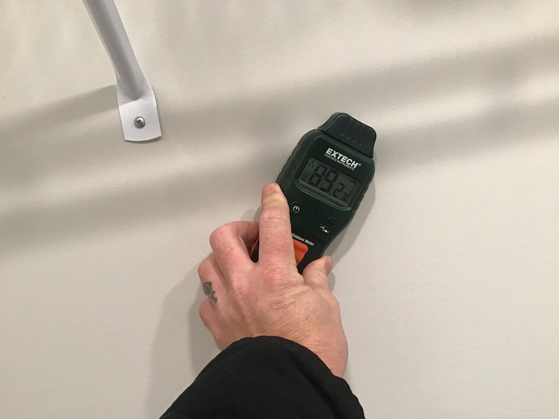 Hand holding a moisture meter against a white wall, measuring 84.2%. Metal bracket visible.
