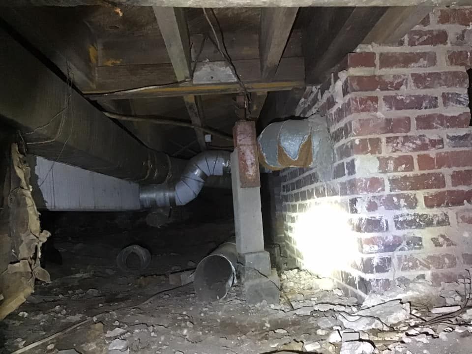 Underneath a building: ductwork, brick support, exposed beams, dark, damp crawlspace.
