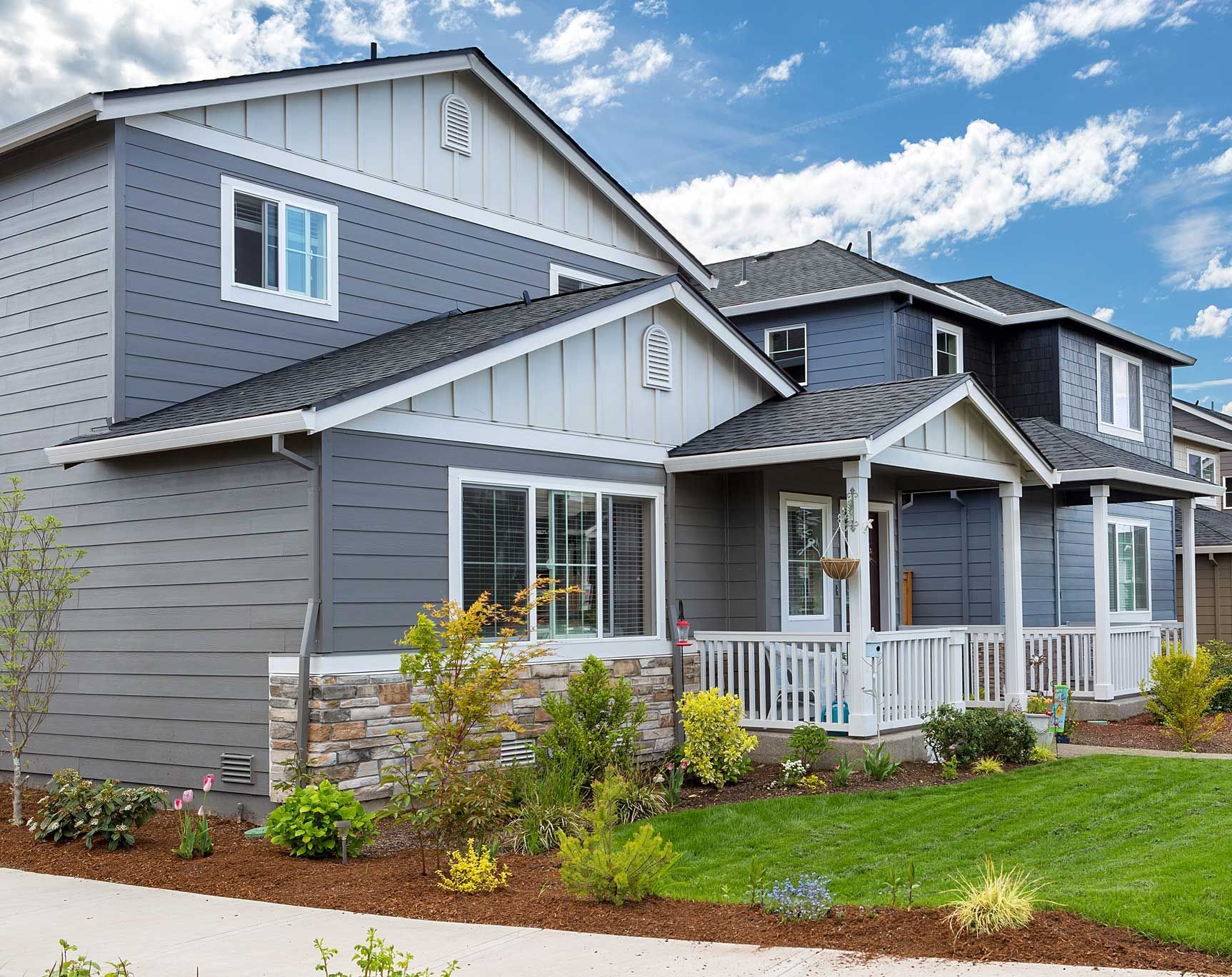 Multi-unit homes with gray and blue siding, white trim, and small front porches, under a blue sky.