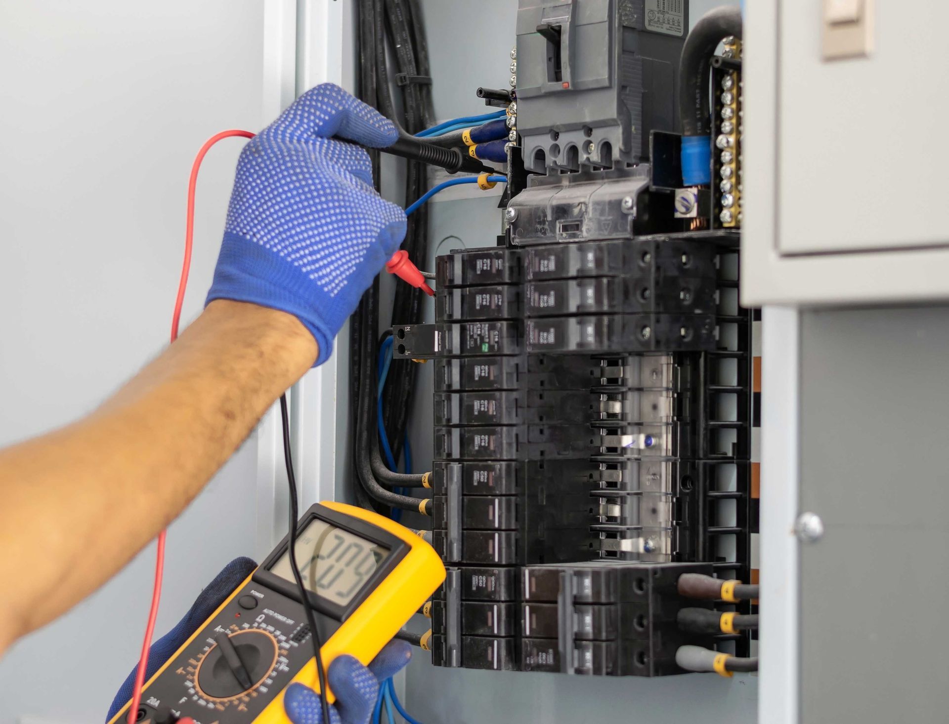 Electrician testing a circuit breaker panel with a multimeter, wearing blue gloves.