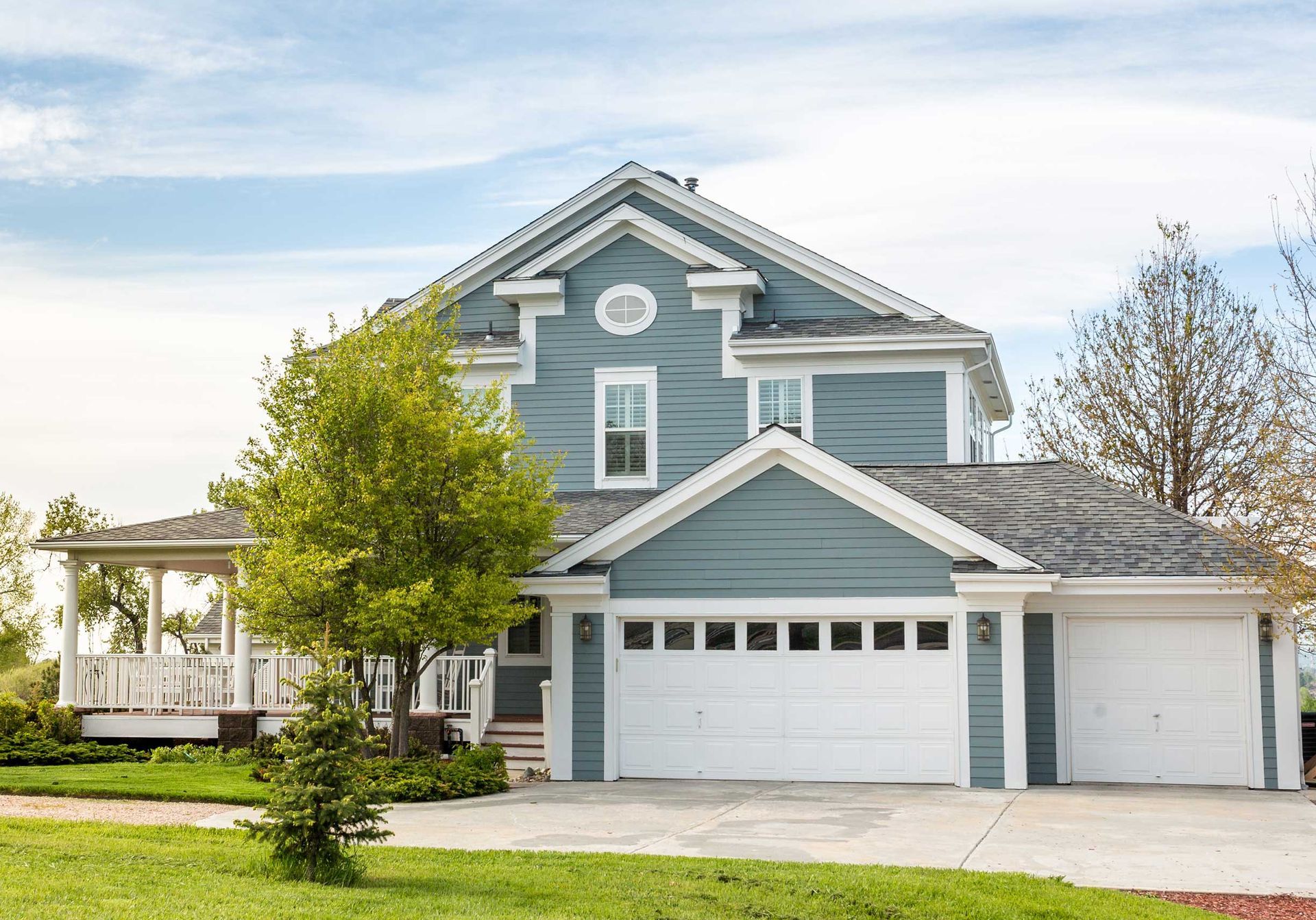 Blue two-story house with white trim, porch, and garage doors, under a blue sky.