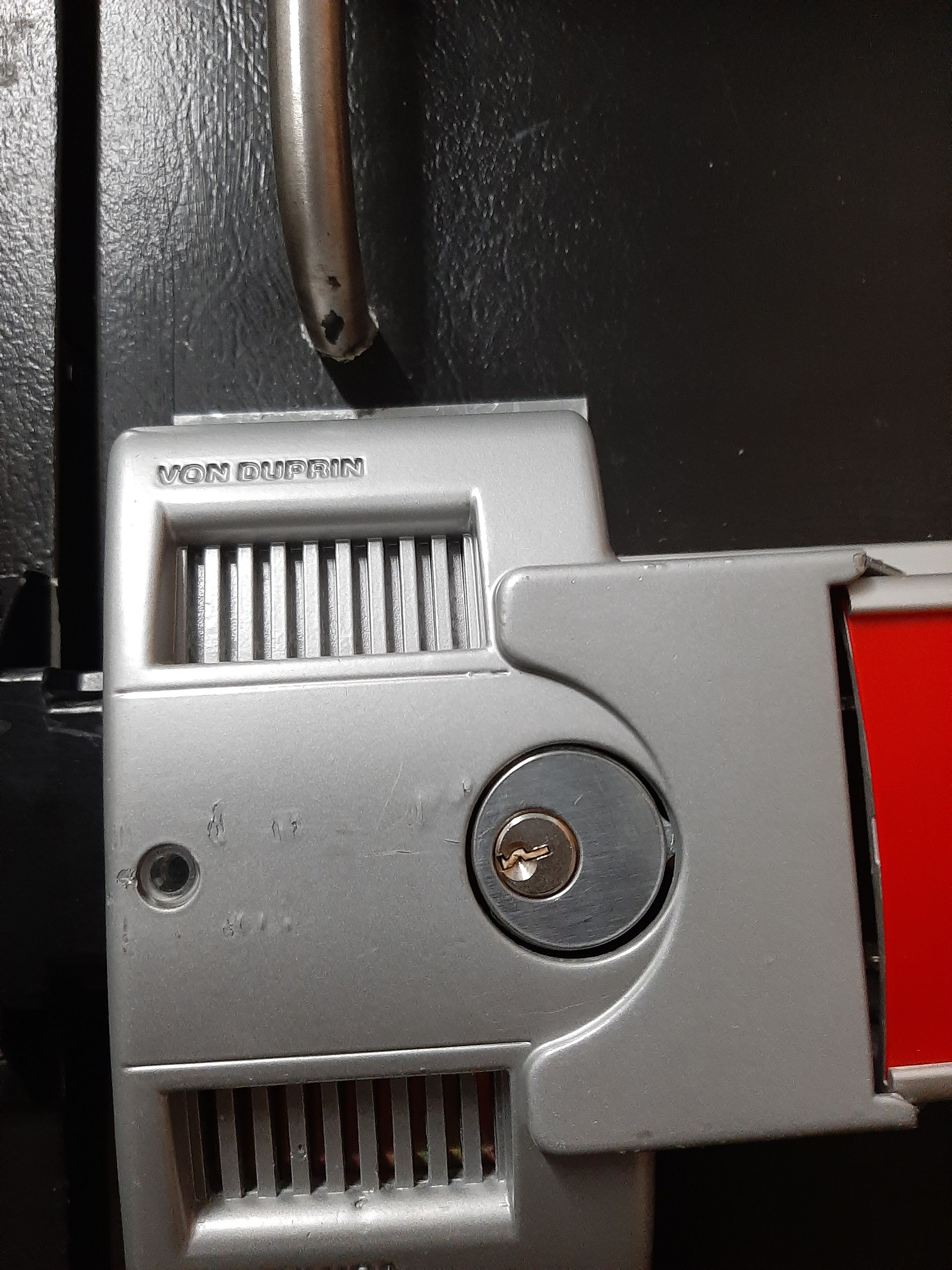 Close-up of a metal latch and screw on a gray device with a red panel.