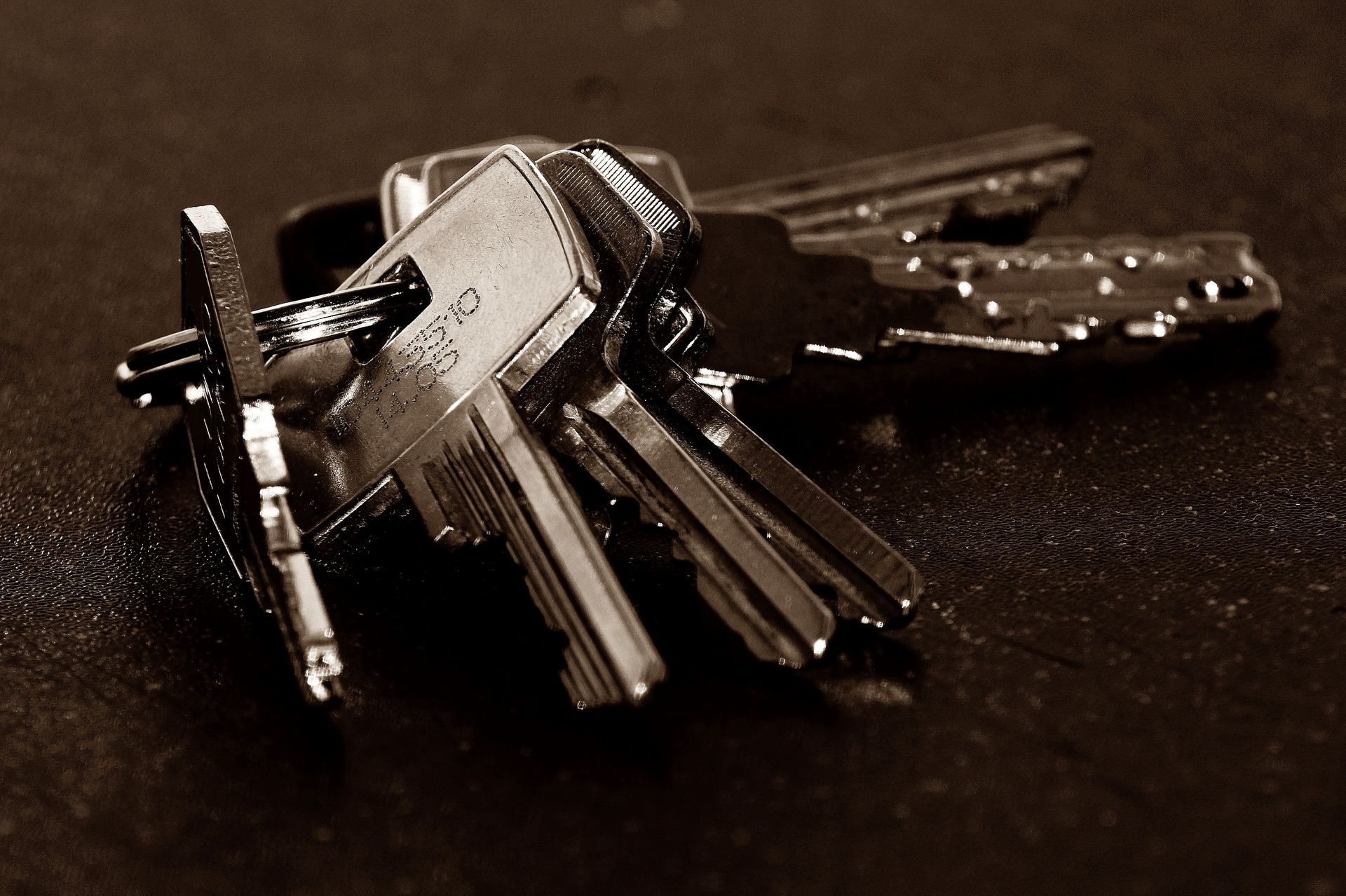 A small set of metal keys on a dark surface, with a keychain ring in front.