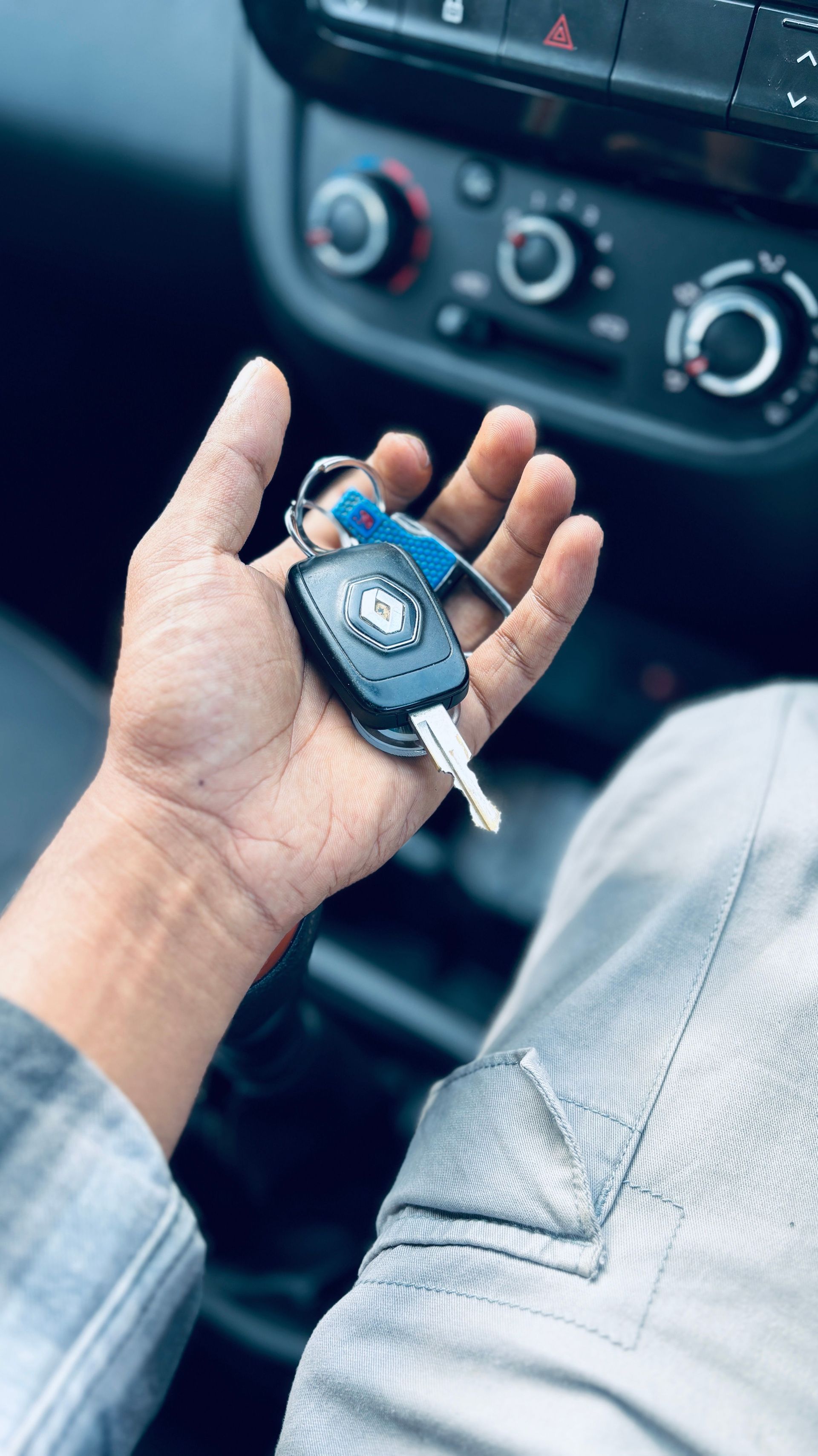 Hand holding a car key fob inside a vehicle, with dashboard controls in the background.