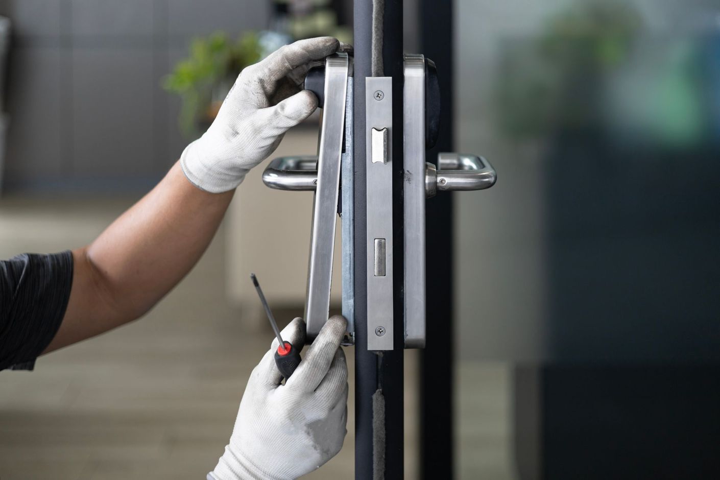 Gloved hands using a screwdriver to repair a glass door lock and handle