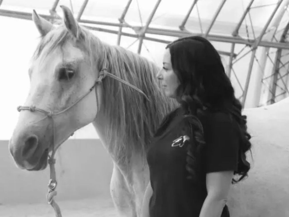 A woman is standing next to a white horse in a black and white photo.