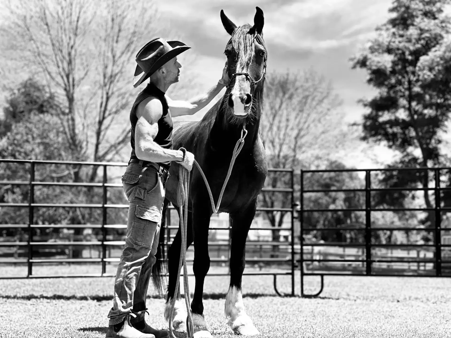 A man in a cowboy hat is petting a horse in a black and white photo.