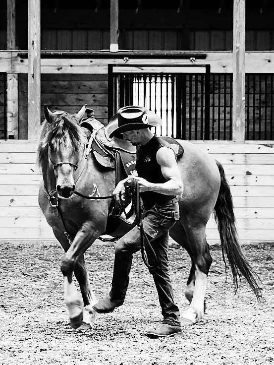 A man in a cowboy hat is walking a horse in a black and white photo.