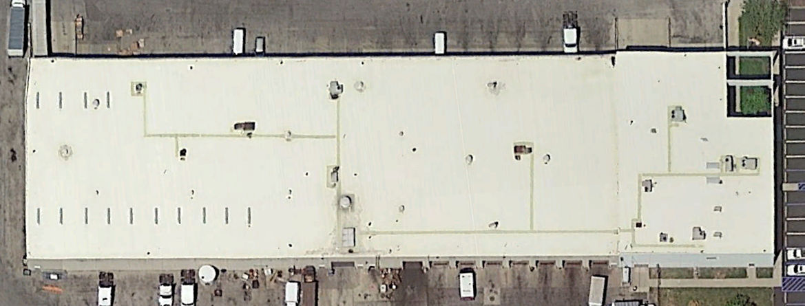 Overhead view of a large, beige-roofed industrial building with a rectangular shape, surrounded by parking lots.