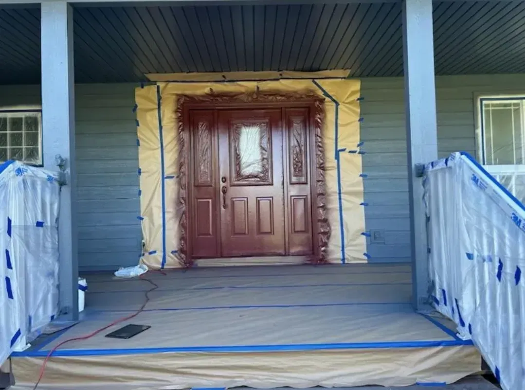Front porch with red-painted door, protective covering on surrounding surfaces, blue trim.