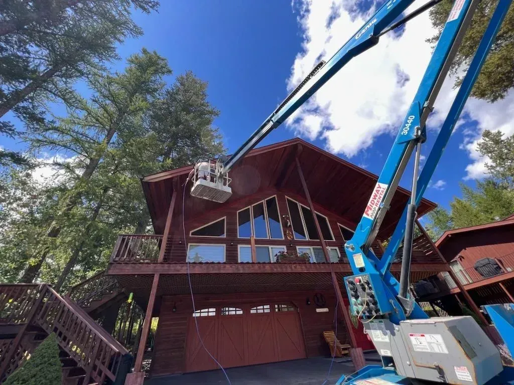 Blue lift bucket near a red cabin with large windows under a blue sky.