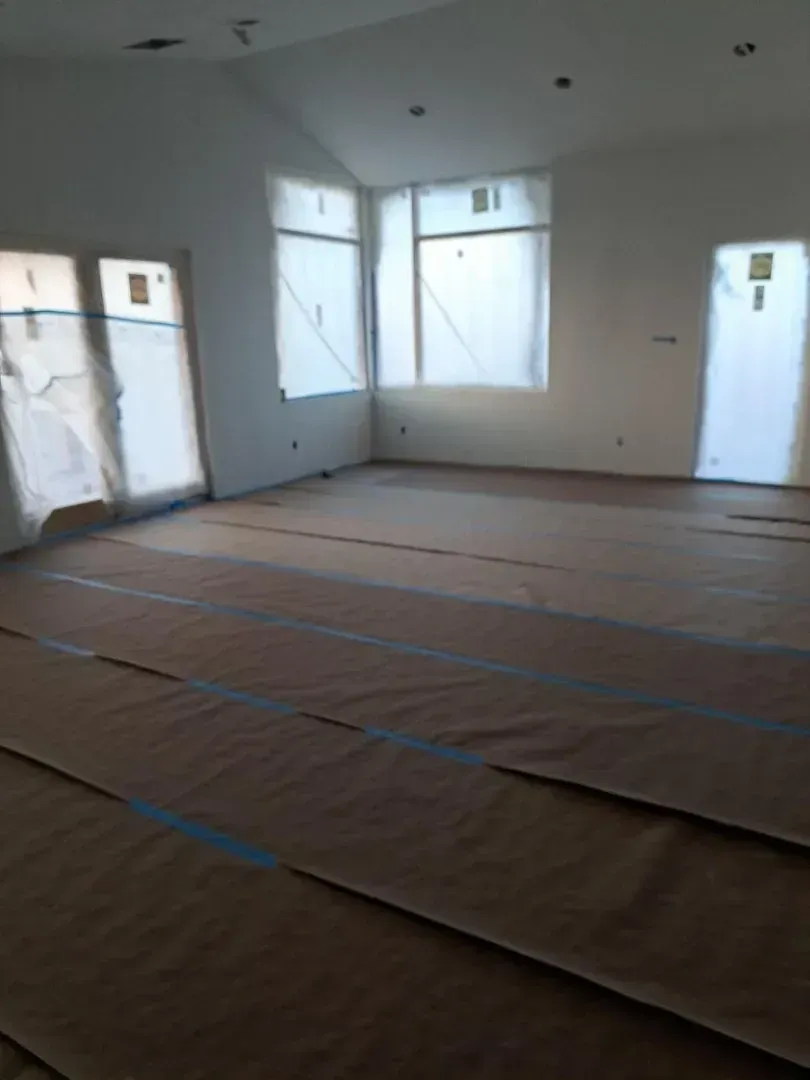 Empty room under construction, with windows covered in plastic, floor covered in protective paper.