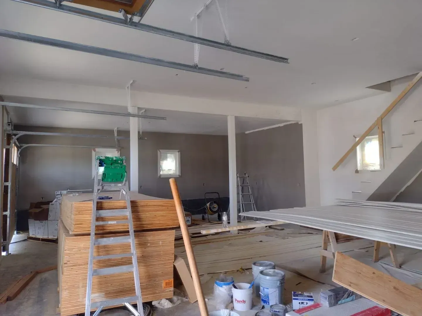 Interior of a building under construction, with exposed beams, lumber, and drywall.