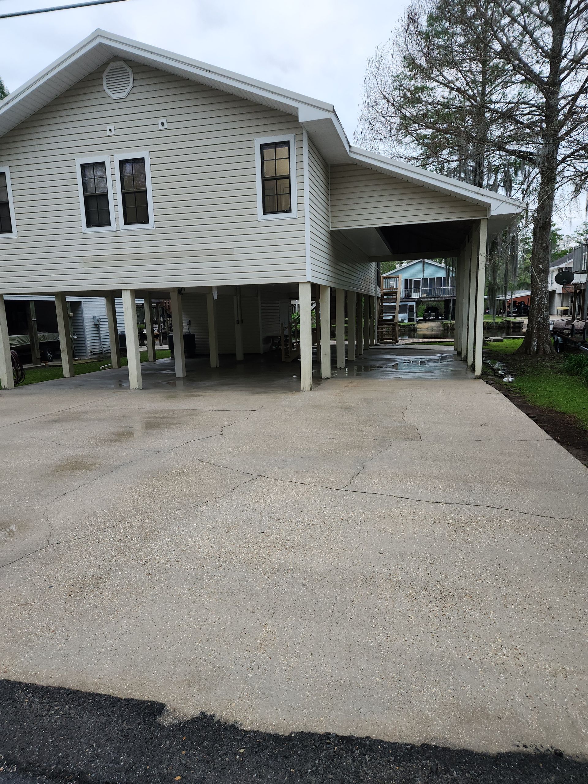 House raised on stilts with a concrete driveway. A carport is on the right. Overcast day.