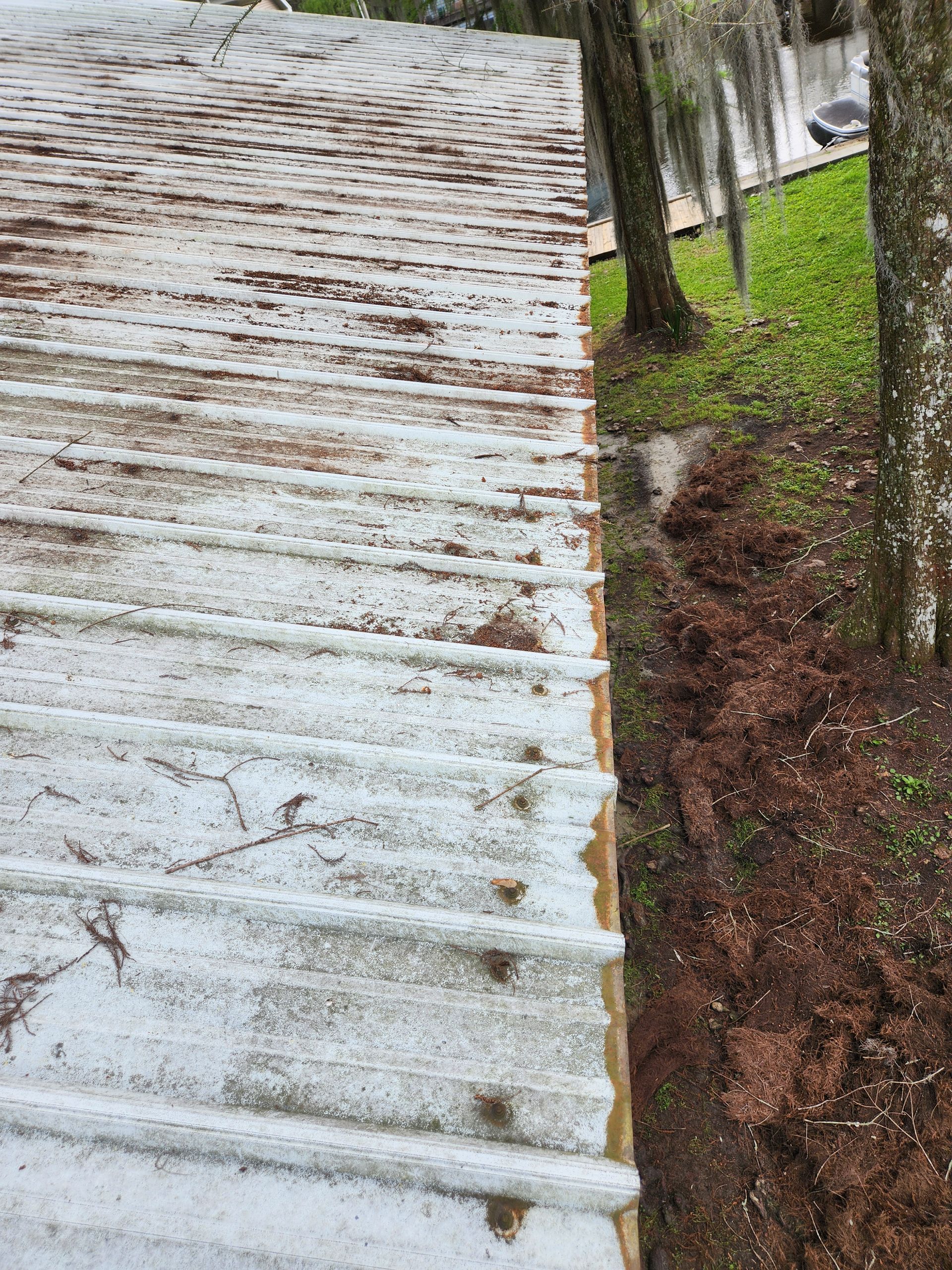 A metal roof covered in debris borders a muddy area next to trees. Brown and white tones dominate the scene.