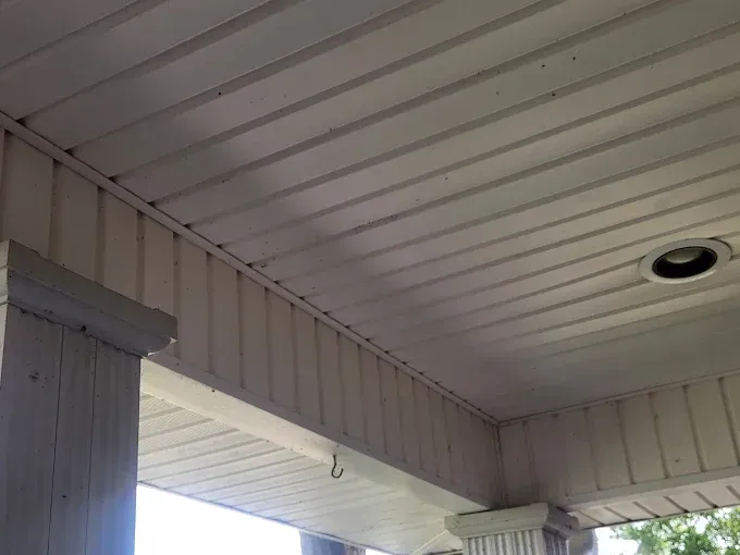 White porch ceiling with horizontal planks and vertical paneling, columns on either side.