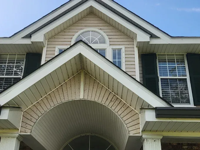Beige and white house exterior with arched entryway, dark shutters, and a blue sky. Staining visible on the entryway.