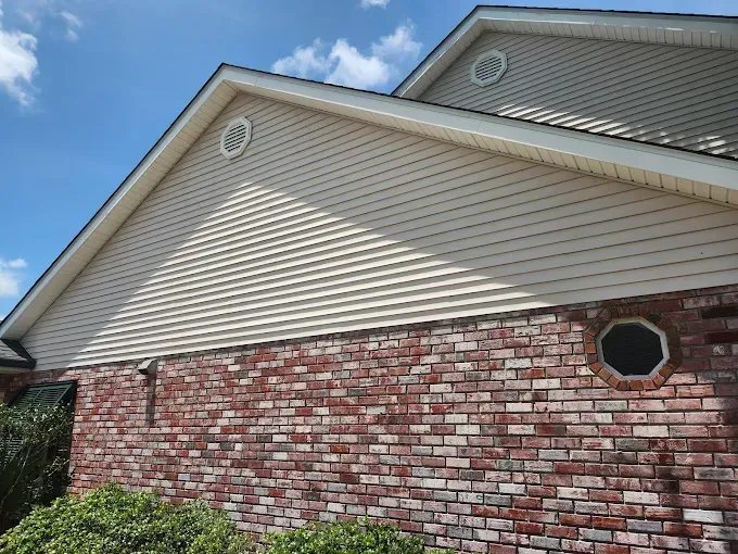Brick and beige siding on a house with a blue sky backdrop. Includes two circular vents and one octagonal window.