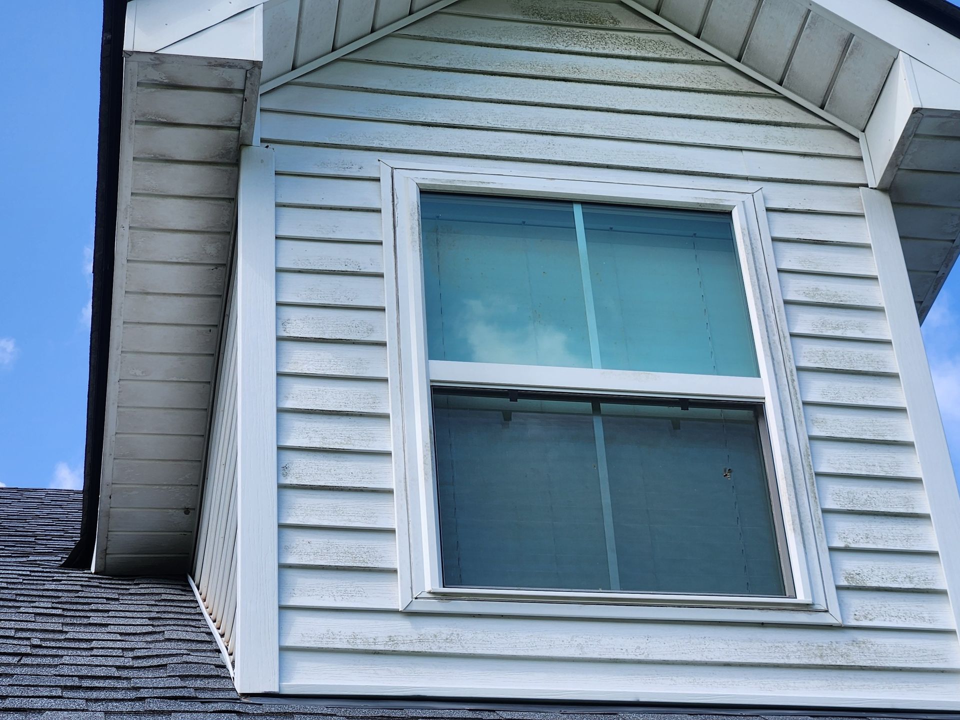 White dormer window on a house with light blue sky visible. The window is outlined with white trim and set into the siding.
