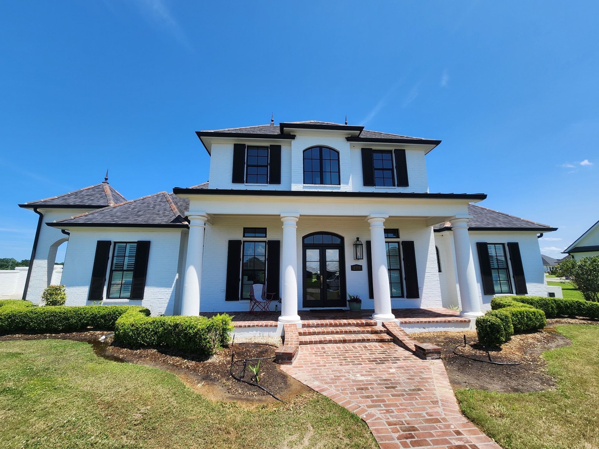 White two-story house with black shutters, a brick pathway, and a blue sky.