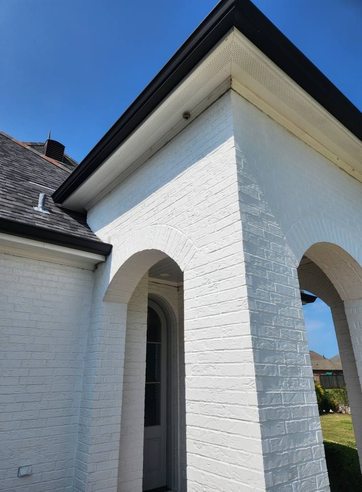White brick building with arched doorways and black roof trim against a bright blue sky.