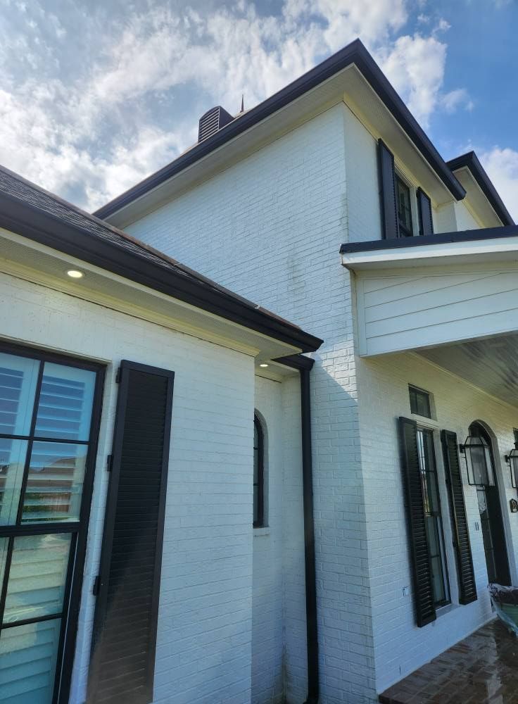 White brick house with black trim, shutters, and gutters, under a cloudy sky.