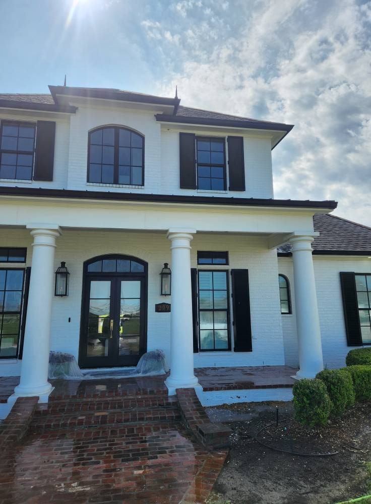 White two-story house with black shutters and trim, a brick walkway, and tall columns under a partly cloudy sky.