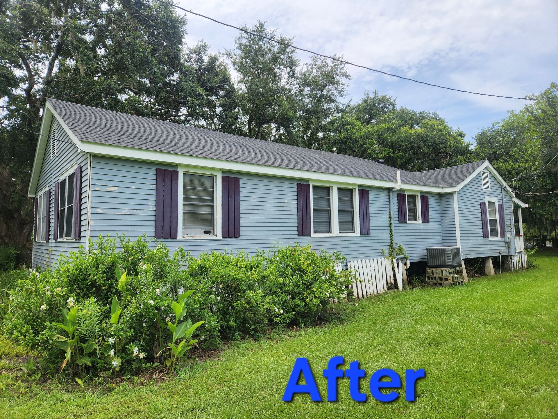 Blue house with purple shutters and a dark gray roof in a grassy setting. 